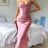 Woman in a pink satin slip dress with a fitted silhouette, standing by a bed