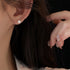 Pearl stud earring worn on ear with glitter nail visible in frame, shown against dark background