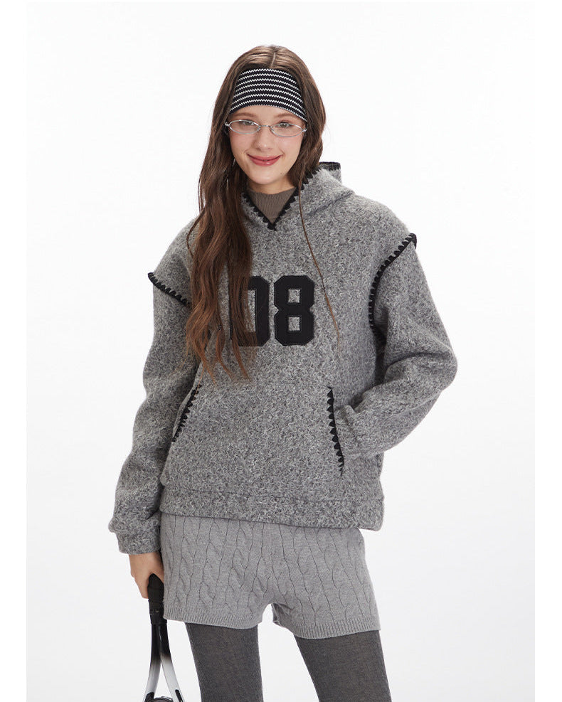 Heather grey textured hoodie featuring large '08' varsity number appliqué in black, black whipstitch trim on hood and pockets, and kangaroo pocket design. Styled with grey cable-knit shorts, grey leggings, and black and white striped headband.