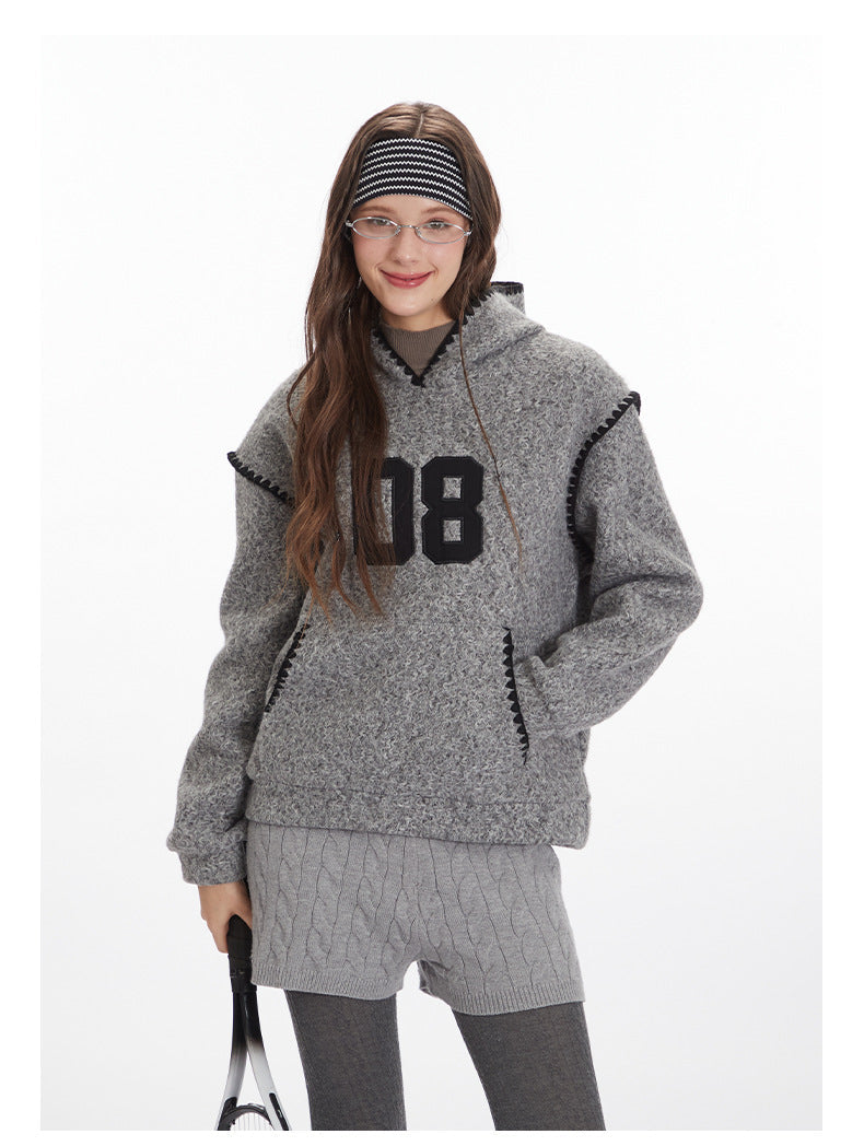 Heather grey textured hoodie featuring large '08' varsity number appliqué in black, black whipstitch trim on hood and pockets, and kangaroo pocket design. Styled with grey cable-knit shorts, grey leggings, and black and white striped headband.