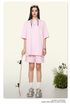 A woman wearing a soft pink oversized t-shirt and shorts set, styled with white socks and chunky sneakers, holding a skateboard against a neutral background with plants
