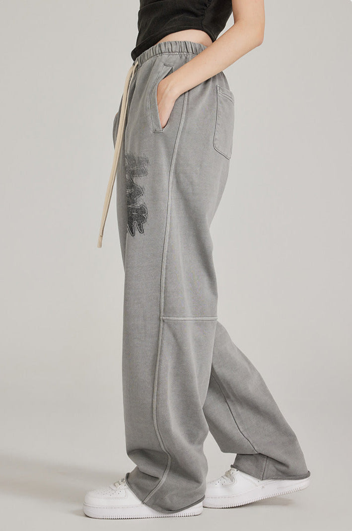 Side angle of model in black crop top with hand in pocket of grey sweatpants featuring graffiti print and white sneakers