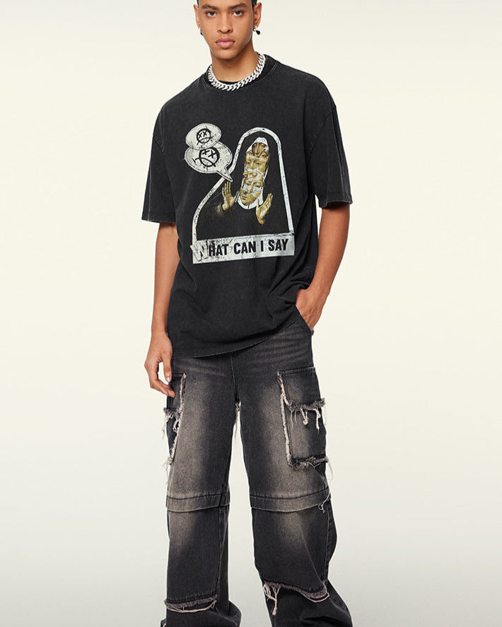 A model posing in a black graphic tee with distressed cargo jeans. Wearing silver chain necklace and styled braids against neutral background