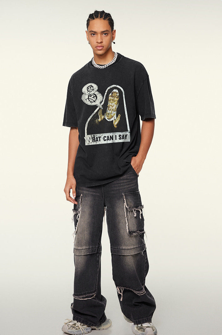 A model posing in a black graphic tee with distressed cargo jeans. Wearing silver chain necklace and styled braids against neutral background