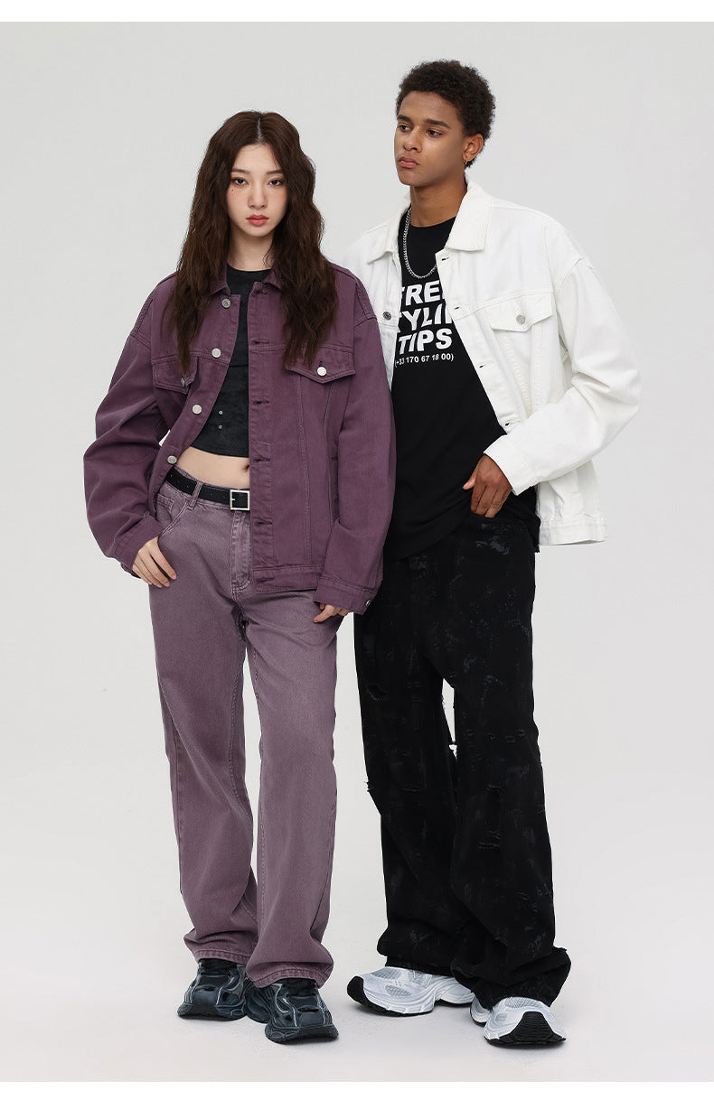 A woman in purple denim jacket and pants stands beside man in white denim jacket and black distressed jeans against white studio backdrop