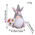 Easter gnome with an 8.27in (21cm) gray knitted hat, pink bunny ears, white beard, and holding white and pink flowers.