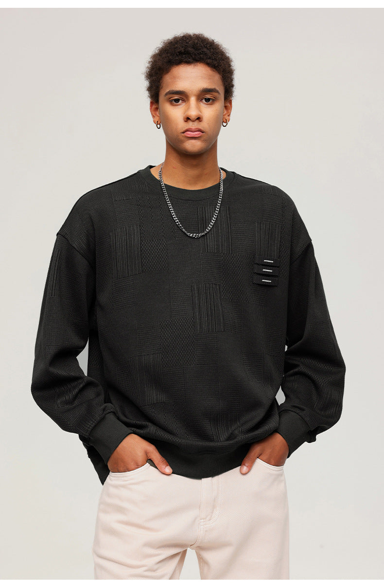 Close-up portrait of male model wearing black textured sweatshirt with decorative tabs and white pants