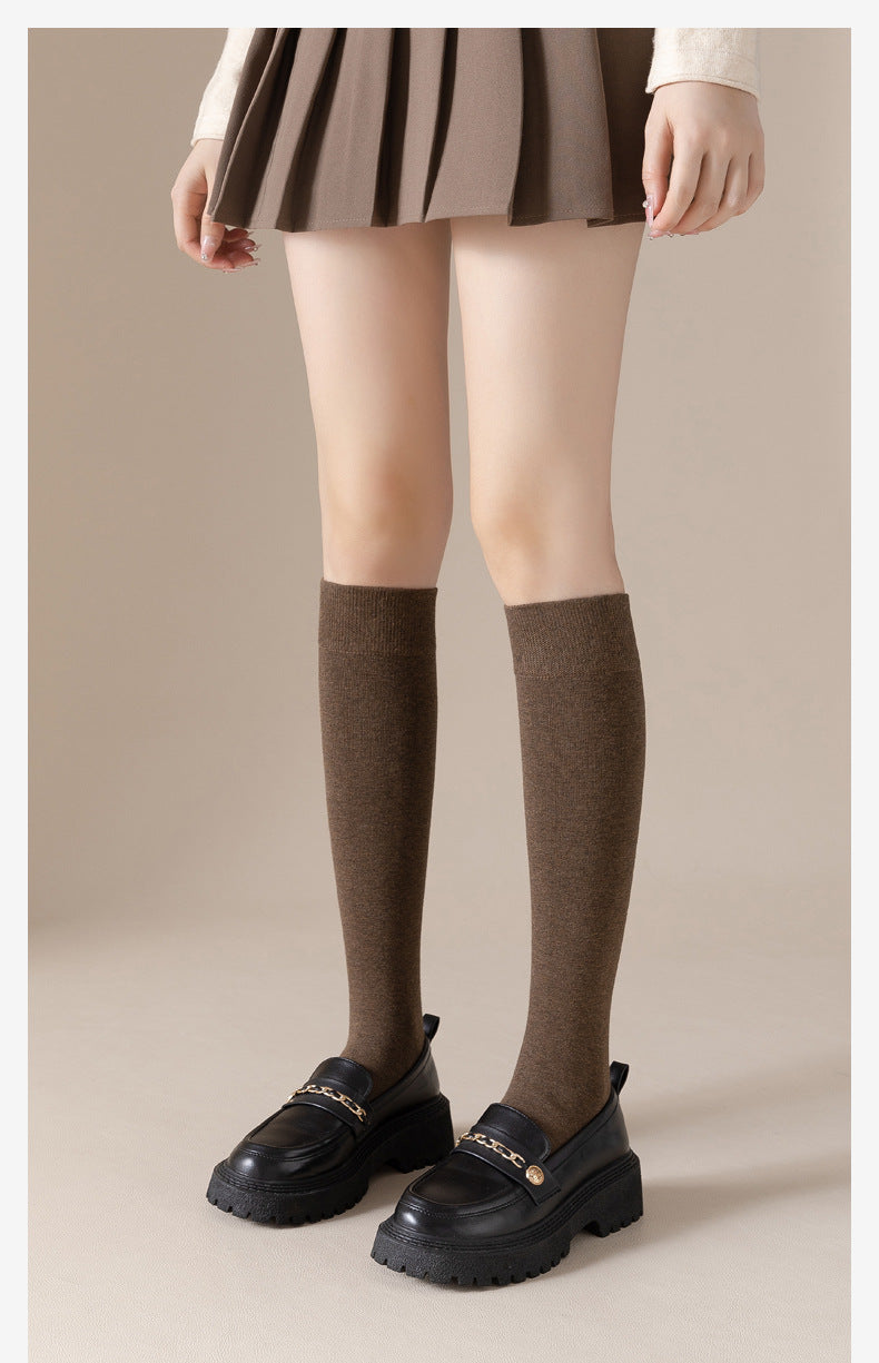Person in pleated skirt and brown knee-socks with black chain-detail loafers