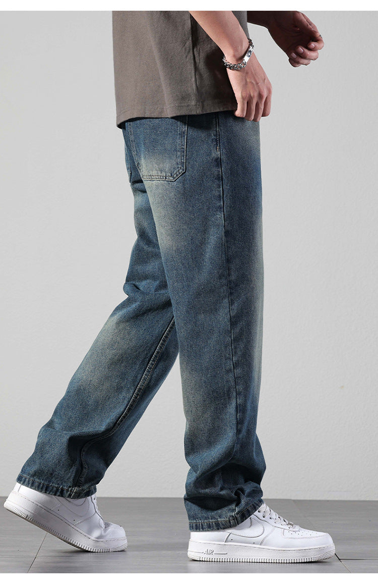 A person wearing wide-leg faded denim jeans with gray oversized t-shirt and silver chain bracelet, styled with white Nike Air Force 1 low sneakers