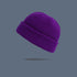 A deep purple ribbed knit beanie with folded cuff floating against slate gray background, displaying classic winter hat design