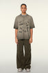 A model with braided hair wearing taupe graffiti-print oversized t-shirt and olive cargo pants standing against white background