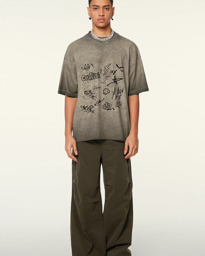 A model with braided hair wearing taupe graffiti-print oversized t-shirt and olive cargo pants standing against white background