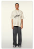 Oversized off-white Beattube t-shirt with distressed logo, wide gray pants, and gray sneakers