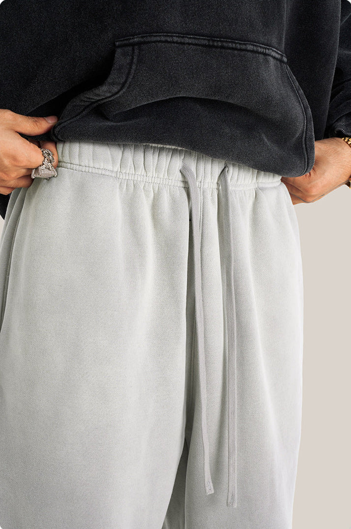 Close-up of elastic waistband detail on light gray sweatpants with drawstring and person lifting black hoodie