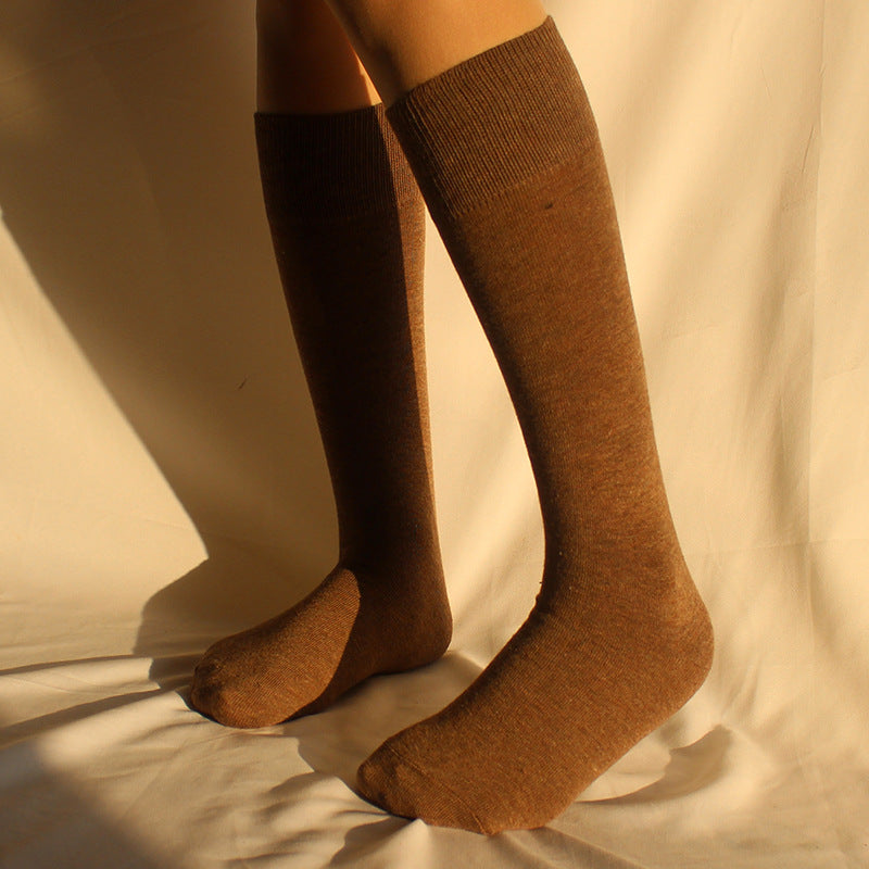 Front view of person wearing knee-high brown cotton socks with ribbed cuffs against cream background with natural lighting