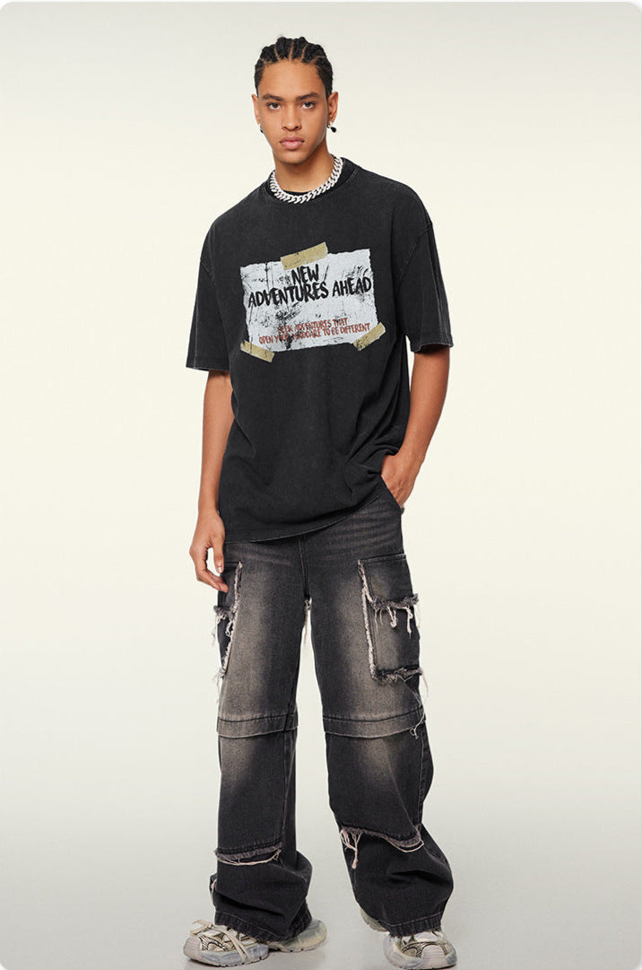 Male model wearing black "New Adventures Ahead" t-shirt with distressed graphic and ripped gray jeans