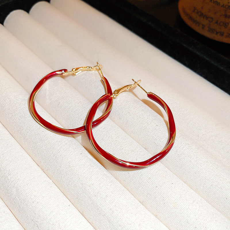 A pair of twisted red enamel and gold hoop earrings is displayed on a white cushioned jewelry tray