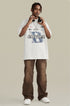 A model wearing white graphic t-shirt with blue 'B' logo and 'Extreme Acceleration' text, paired with brown pants, headphones and silver chain