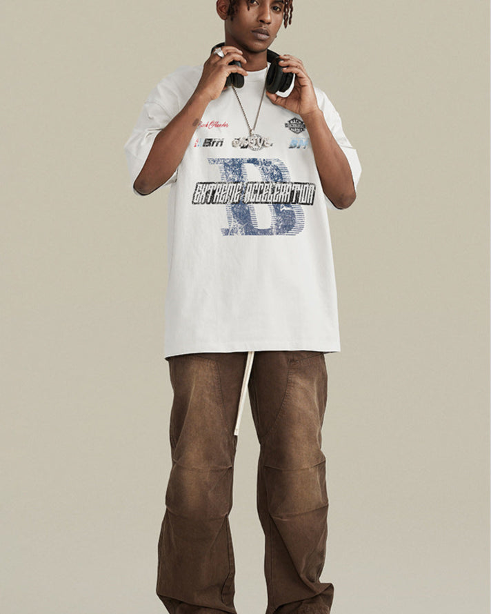 A model wearing white graphic t-shirt with blue 'B' logo and 'Extreme Acceleration' text, paired with brown pants, headphones and silver chain