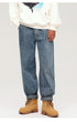 A model wearing wide-leg medium-wash jeans with cuffed hems, white hoodie and tan work boots, standing against white background