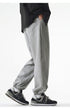A model is wearing gray jogger sweatpants with an elastic waistband and relaxed fit, walking while styled with a black varsity jacket and black New Balance sneakers