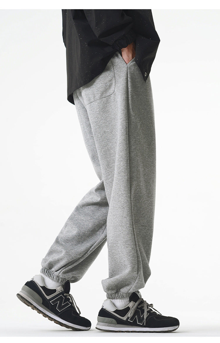 A model is wearing gray jogger sweatpants with an elastic waistband and relaxed fit, walking while styled with a black varsity jacket and black New Balance sneakers