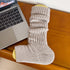 Light beige ribbed leg warmer displayed on yellow cardholder next to MacBook laptop on wooden desk