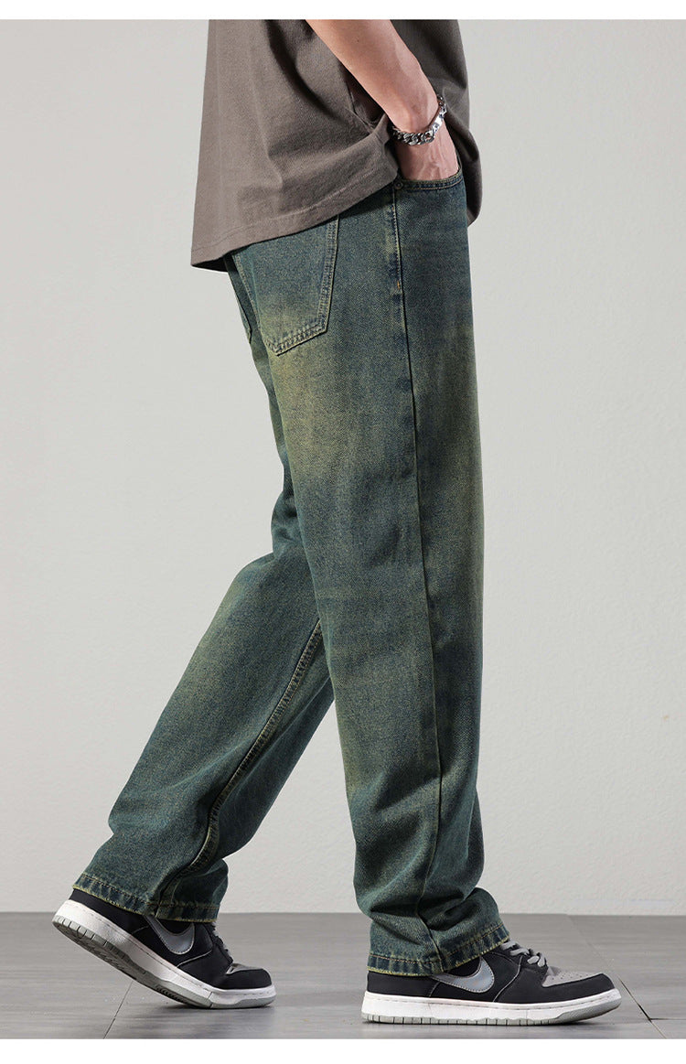 A close-up of a man's faded green-blue denim jeans, emphasizing the front pocket, waistband, and button closure