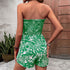 Back view of a woman in a green strapless romper, showing smocked detailing and flowing shorts.