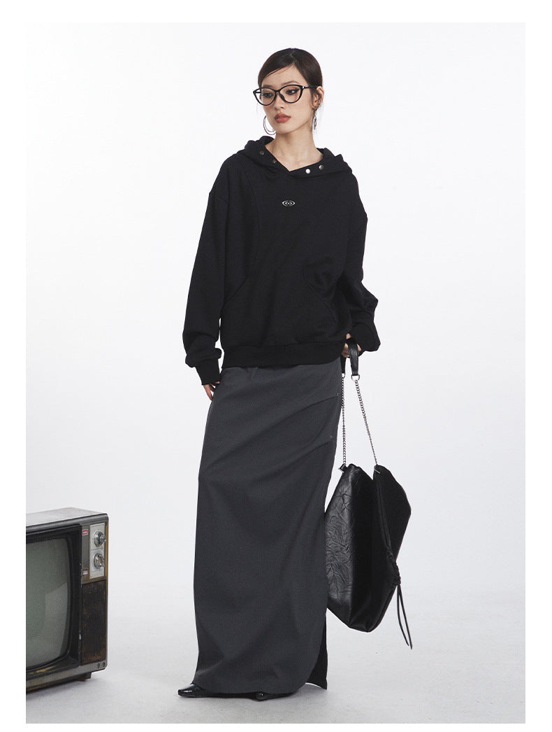 Oversized black hoodie featuring eye logo and metal snap details, styled with charcoal maxi skirt and black leather tote bag