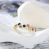 A gold 925 sterling silver bubble ring with rainbow gemstones displayed on white ceramic dish against printed text
