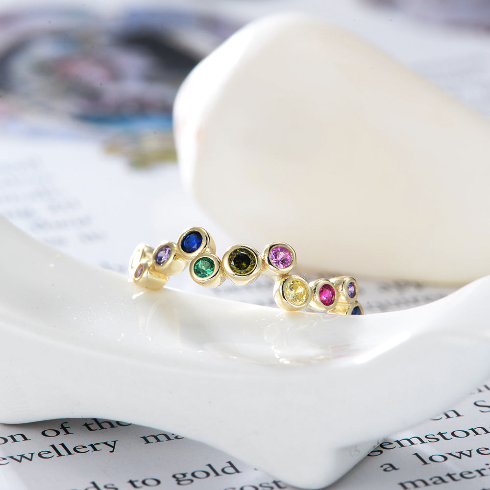 A gold 925 sterling silver bubble ring with rainbow gemstones displayed on white ceramic dish against printed text