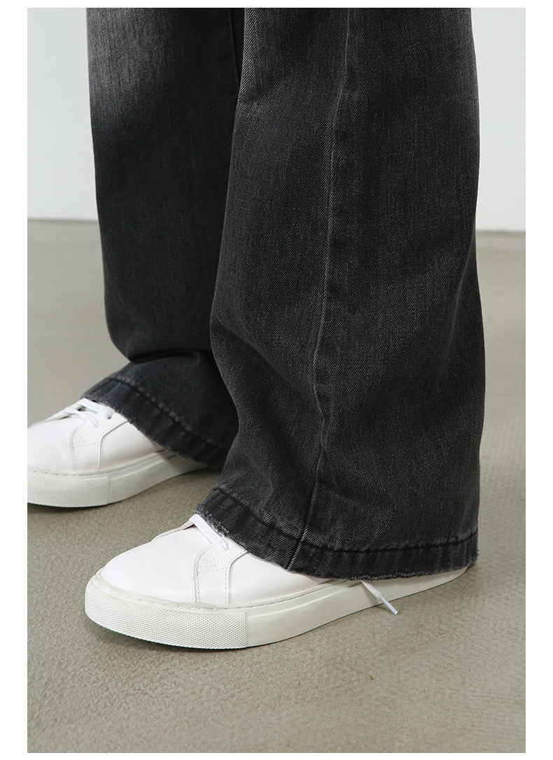 Detail shot of black wide-leg jeans showing seam construction and white sneakers on concrete floor background