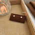 A pair of classic pearl stud earrings on a wooden display, labeled "6mm," placed in a woven tray next to a glass.