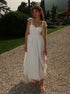 Woman in a white dress standing on a gravel path with greenery and mountains in the background