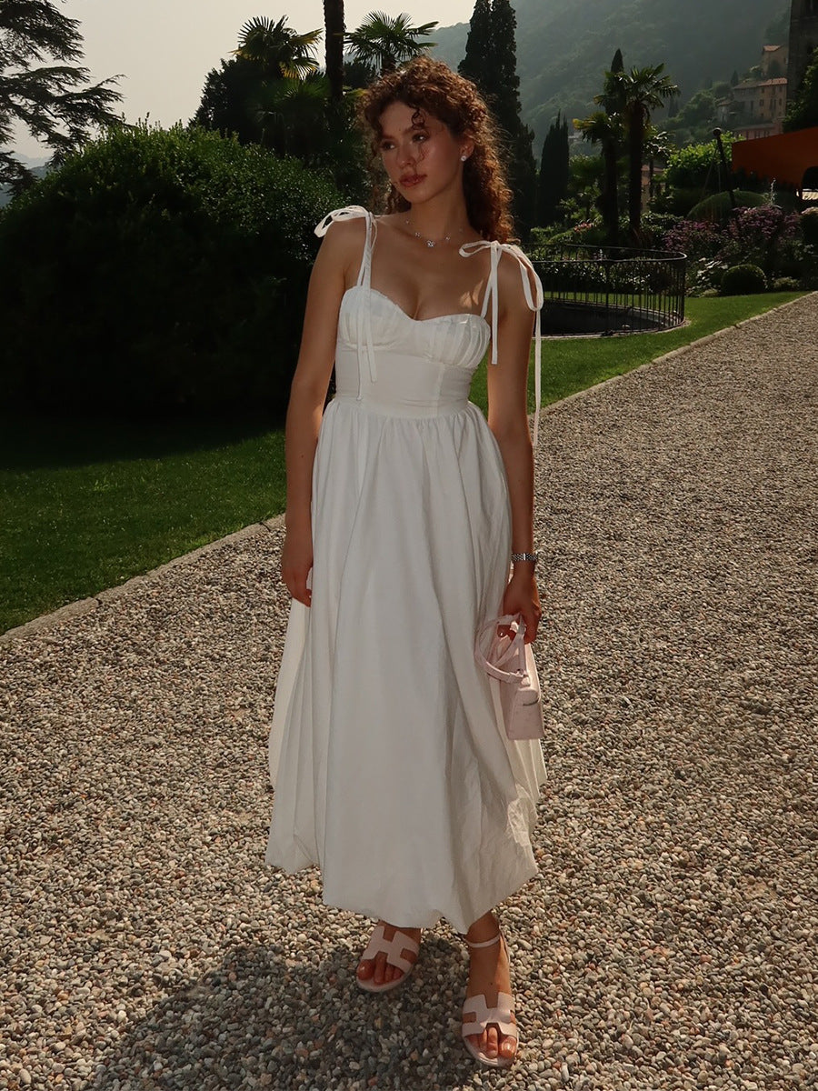 Woman in a white dress standing on a gravel path with greenery and mountains in the background