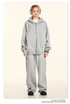 Model with blonde braids wearing oversized light gray zip hoodie, matching baggy sweatpants, headphones, white background