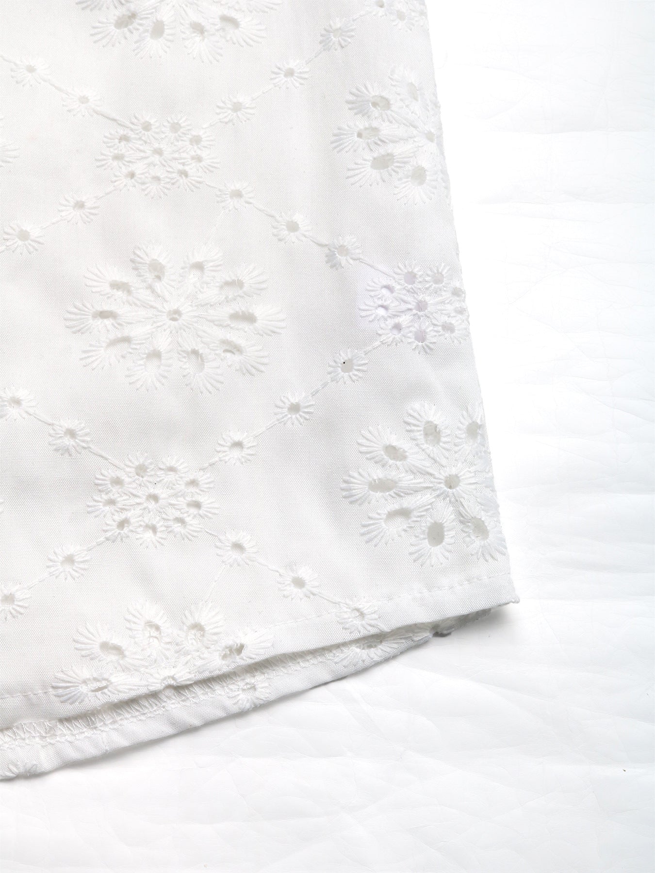 Hemline close-up of white embroidered blouse, showing floral cutout pattern and scalloped edges.