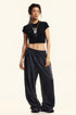 Model poses in a black graphic cropped T-shirt and oversized sweatpants, styled with a pendant necklace and sneakers
