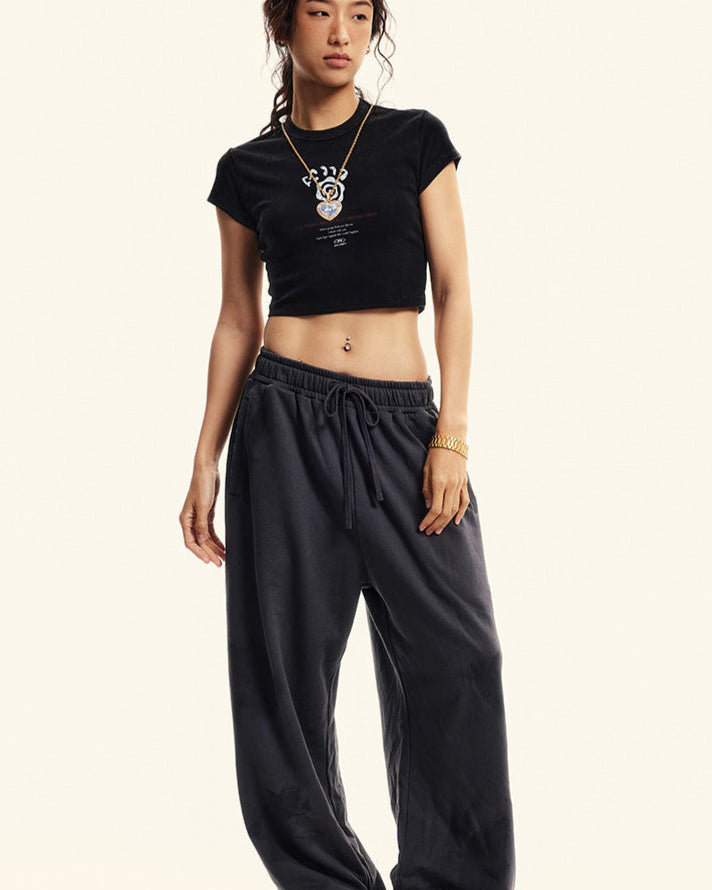 Model poses in a black graphic cropped T-shirt and oversized sweatpants, styled with a pendant necklace and sneakers