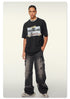 Model wearing black oversized graphic t-shirt with 'NEW ADVENTURES AHEAD' print and distressed gray cargo jeans against neutral background
