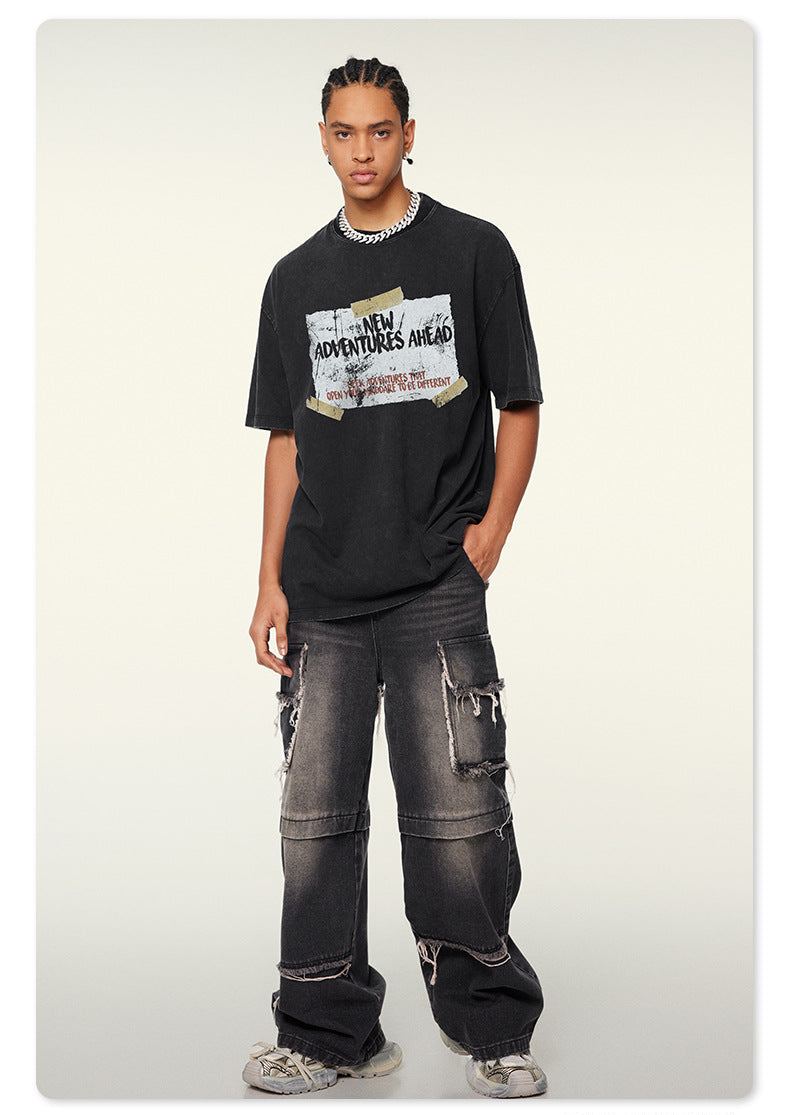 Model wearing black oversized graphic t-shirt with 'NEW ADVENTURES AHEAD' print and distressed gray cargo jeans against neutral background