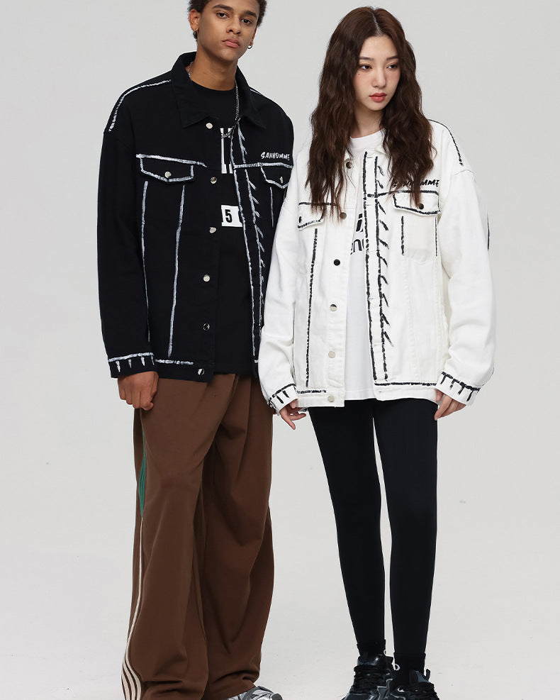 A man and woman are posing on a gray backdrop. He wears black outline jacket with brown pants, she wears white outline denim jacket with leggings