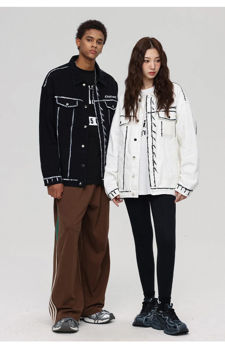 A man and woman are posing on a gray backdrop. He wears black outline jacket with brown pants, she wears white outline denim jacket with leggings