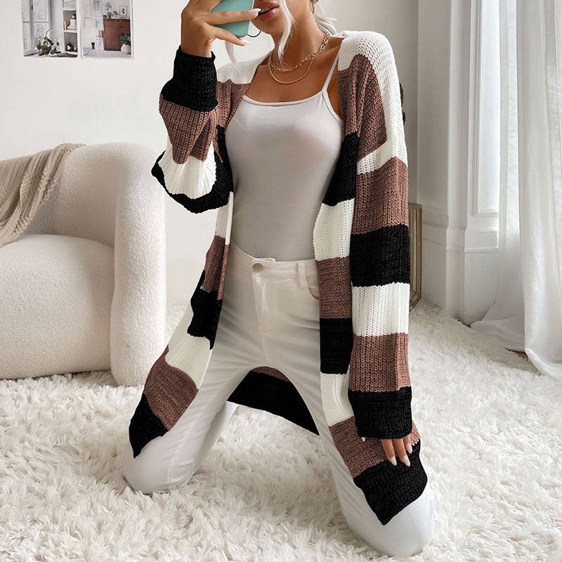 A woman kneeling on white rug showing black and cream striped cardigan with white tank top, holding phone for mirror selfie