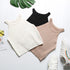Flatlay of three ribbed halter crop tops in white, black and beige, styled with monstera leaf and white sneakers