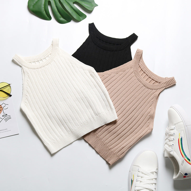 Flatlay of three ribbed halter crop tops in white, black and beige, styled with monstera leaf and white sneakers