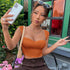 Woman taking a selfie while wearing an orange ribbed crop top with cap sleeves and a sweetheart neckline, accessorized with gold jewelry and sunglasses