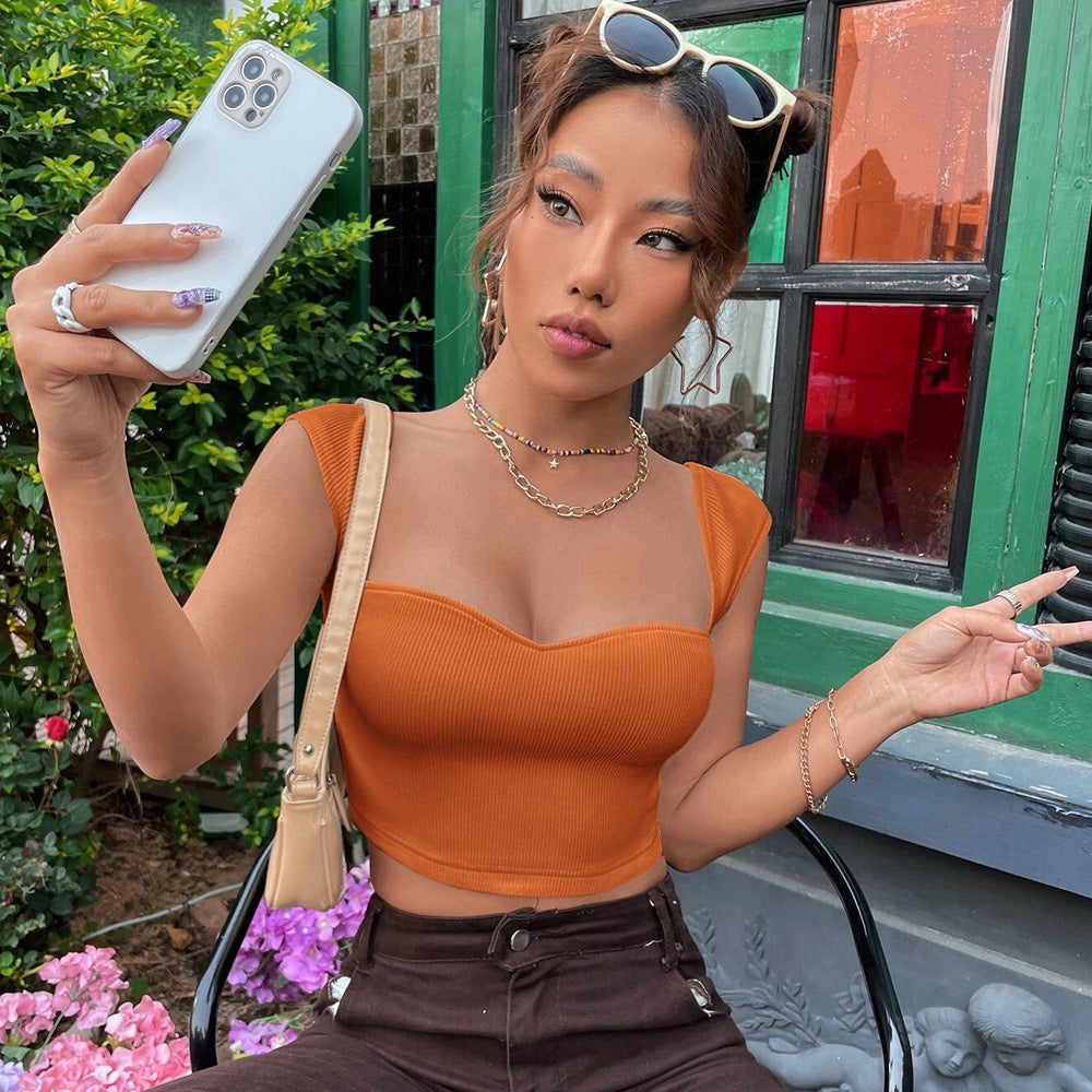 Woman taking a selfie while wearing an orange ribbed crop top with cap sleeves and a sweetheart neckline, accessorized with gold jewelry and sunglasses