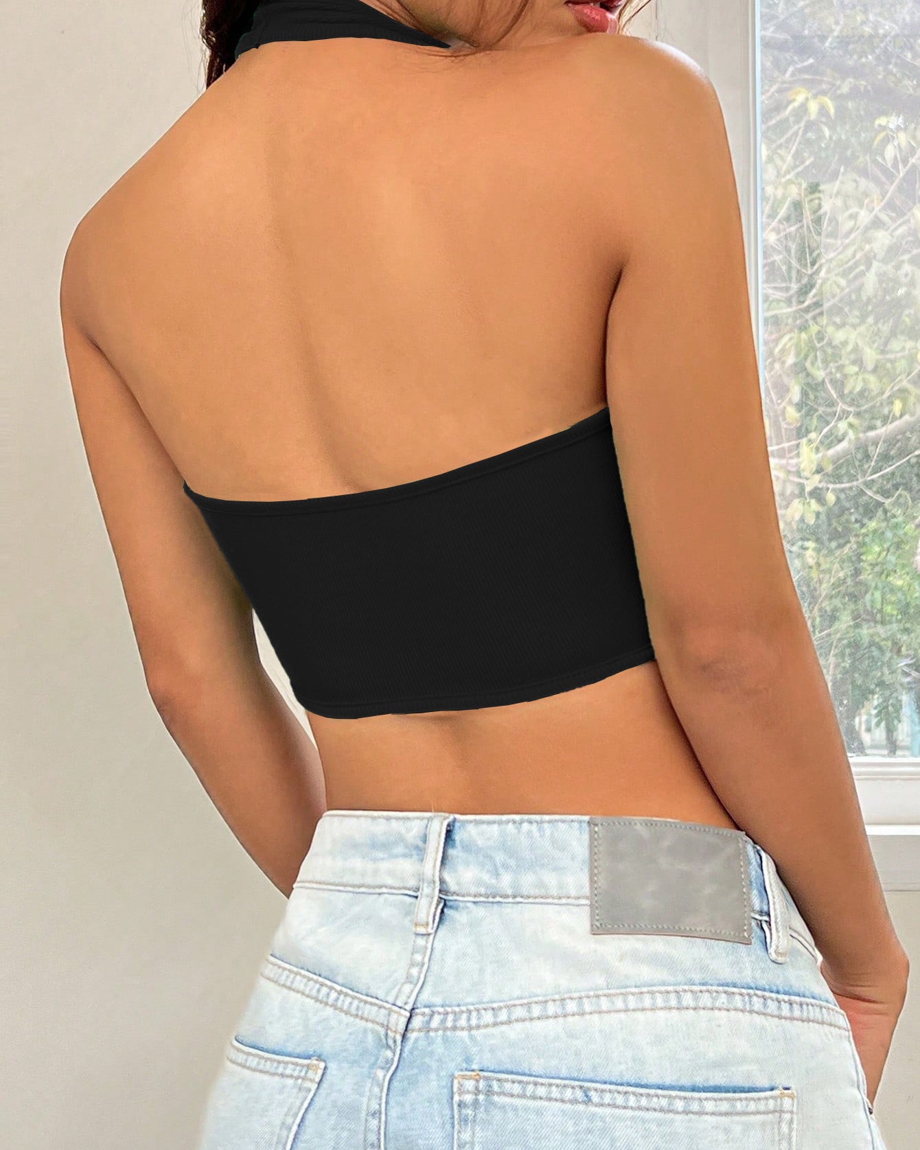 Back view of black ribbed halter crop top with contour seams, paired with light wash denim